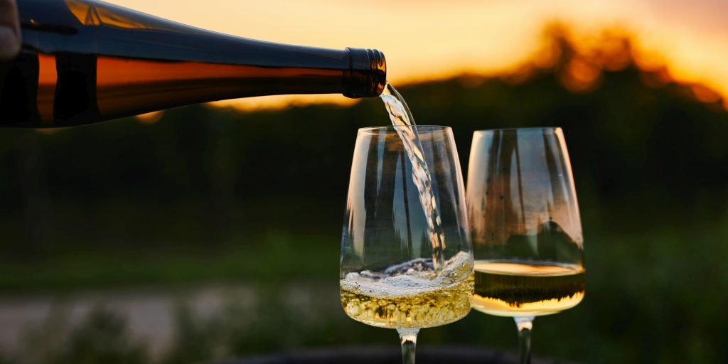 Pouring white wine into glasses in the vineyard at sunset